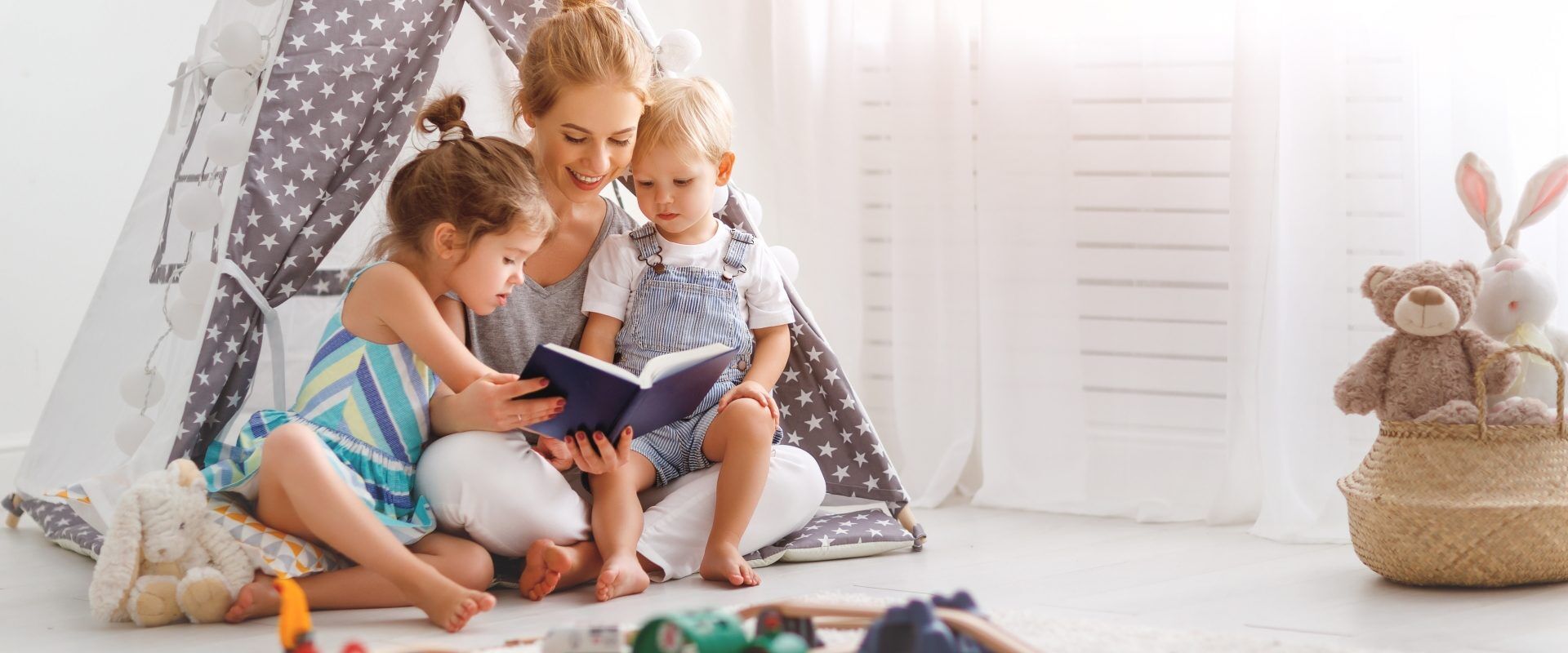 Bajki dla dzieci do wspólnego czytania. Mama z dwójką dzieci siedzą w tipi i czytają wspólnie książkę dla dzieci.