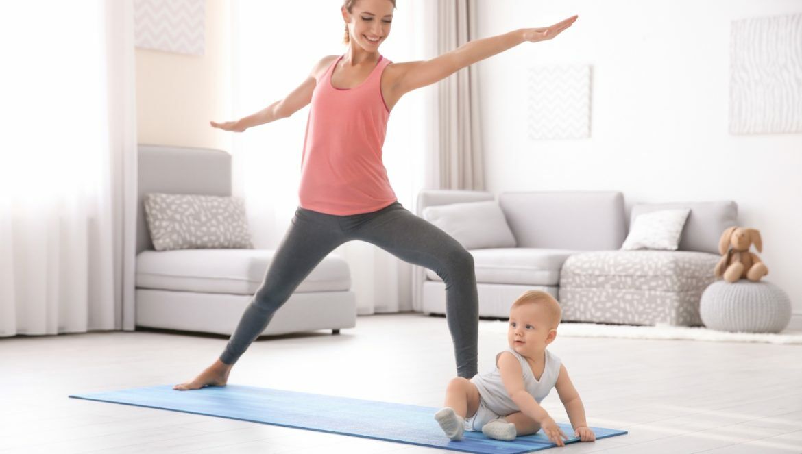 Brzuch po porodzie - jak zrzucić brzuch po ciąży? Młoda mama ćwiczy jogę z niemowlakiem na macie w domu.