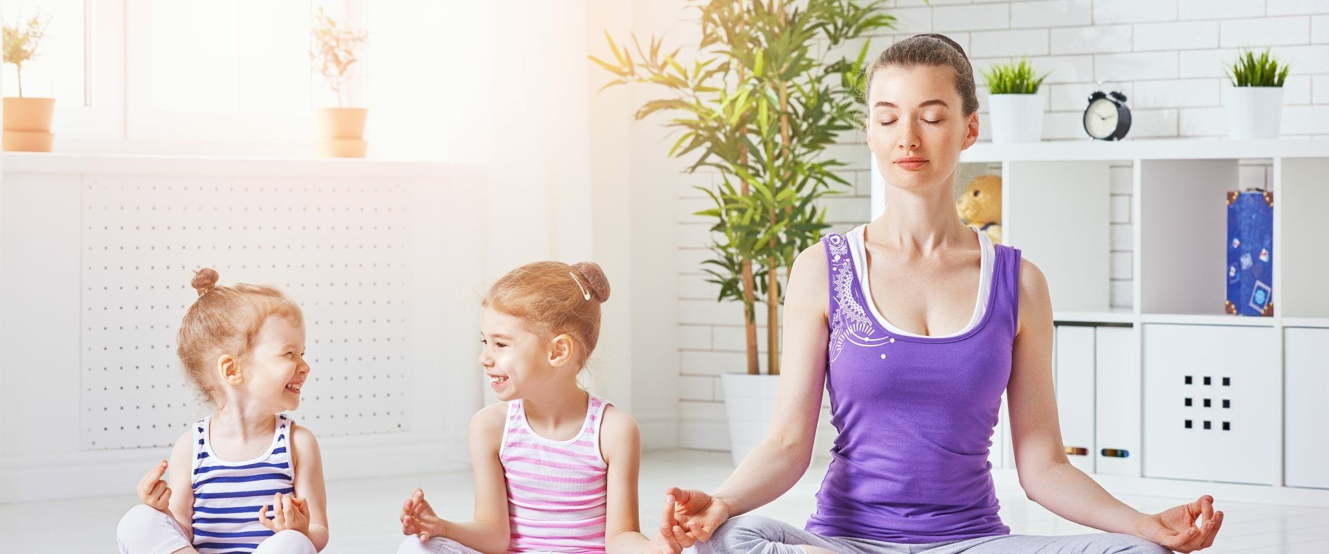Ćwiczenia relaksacyjne dla dzieci - jak wygląda relaksacja dla dzieci? Mama z dwiema córeczkami medytuje na macie w domu.
