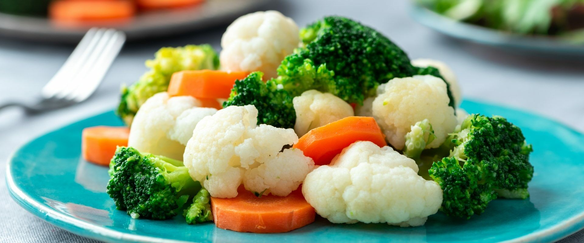 Warzywa gotowane na parze: marchewka, kalafior, brokuł na niebieskim talerzu - dieta przeciwgrzybicza.