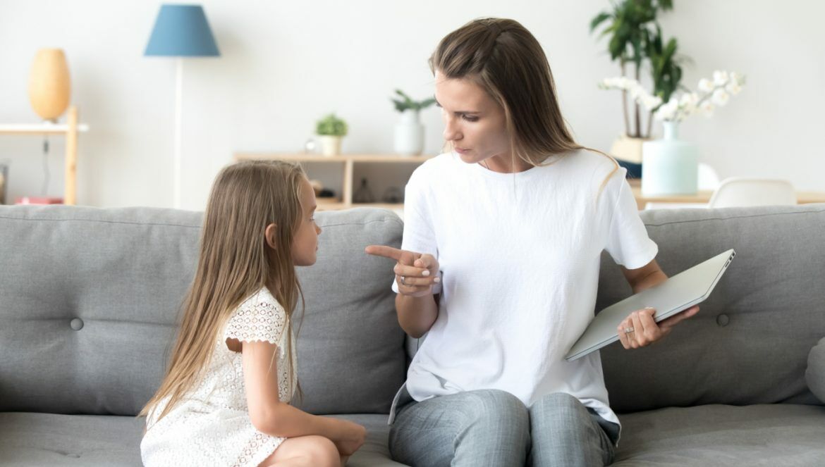 Jak reagować na złość u dziecka? Mama poucza córeczkę, jak powinna się zachowywać, obie siedzą na szarej kanapie w domowym salonie.