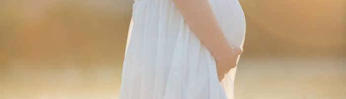 Jak dbać o siebie w ciąży według tradycyjnej medycyny chińskiej? Kobieta w ciąży w białej sukience boho spaceruje po łące.