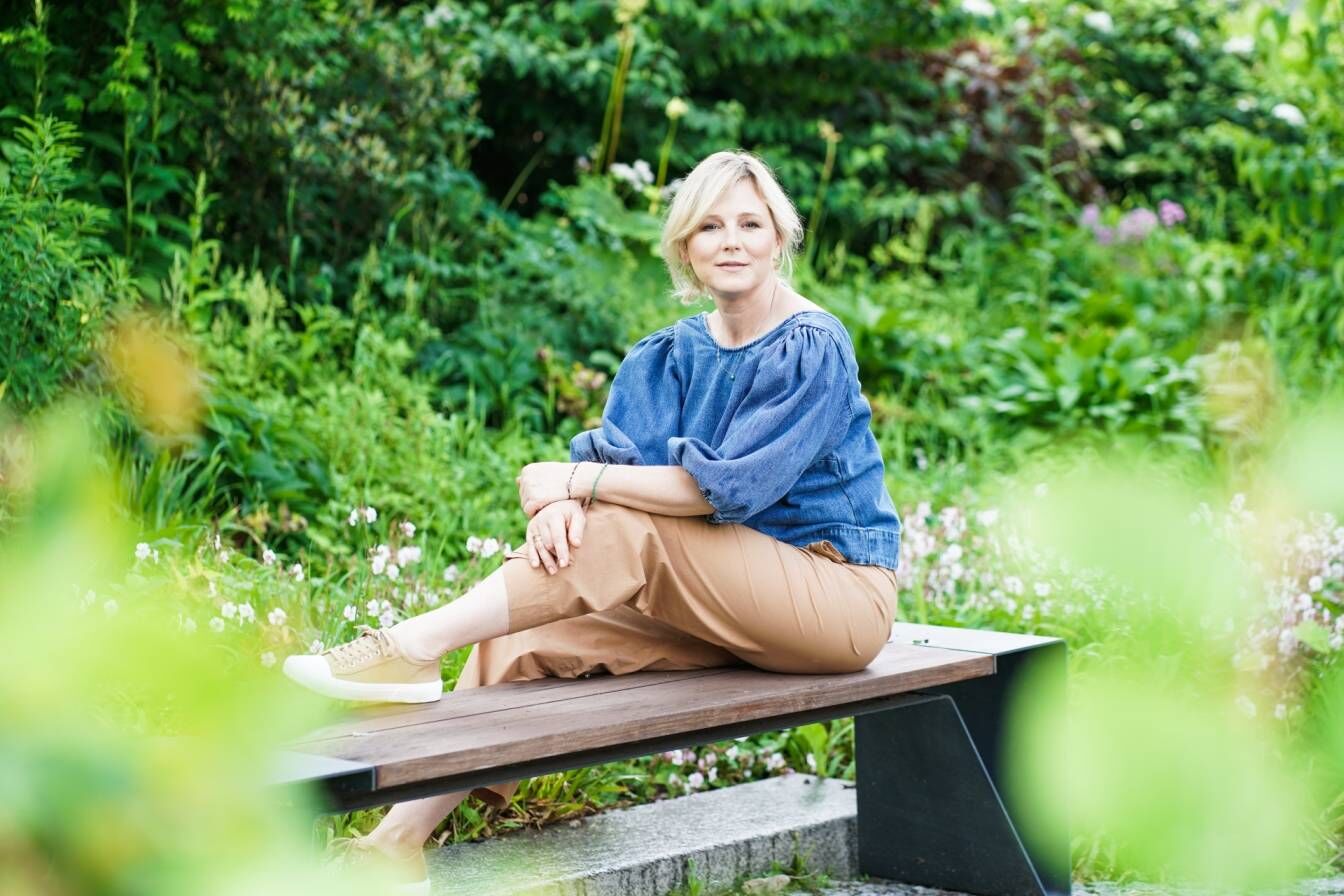 Maja Popielarska siedzi na ławce w ogrodzie.