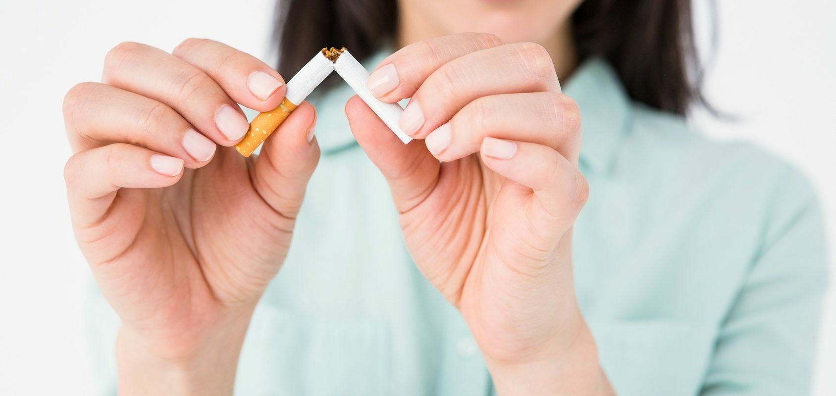 Jak rzucić palenie w 7 krokach? Jakie są sposoby na rzucenie palenia papierosów? Kobieta w błękitnej koszuli przepoławia papierosa na znak rzucenia nałogu.