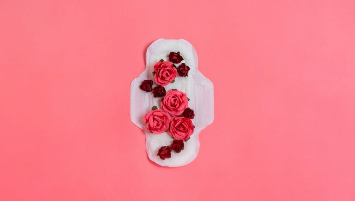 Ubóstwo i wykluczenie menstruacyjne - czym jest i kogo dotyka? Podpaska pokryta płatkami różowych i czerwonych kwiatów na różowym tle.