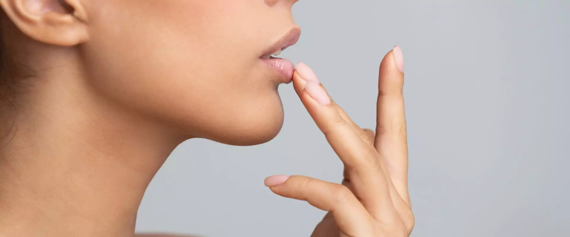 Zmiany na ustach - o czym świadczą? Kobieta dotyka palcem ust.